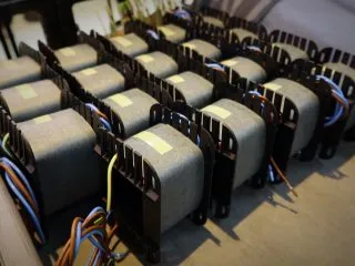 Row of electrical transformers with laminated cores and connected wiring during assembly