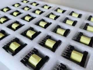 Tray of ferrite transformers with yellow-taped cores on pinned bobbins