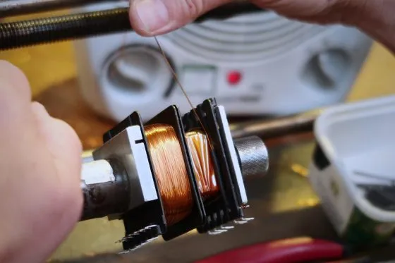Hands guiding copper wire onto a bobbin on a coil-winding machine